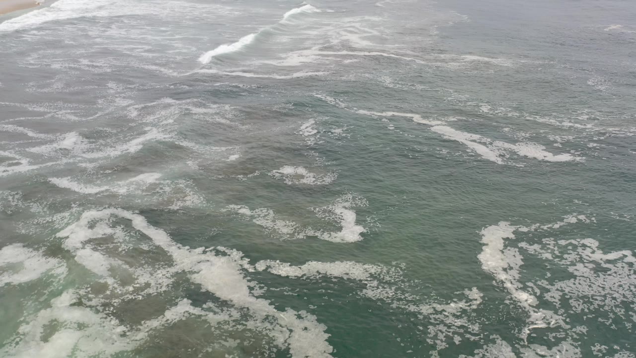 Waves and foam moving across shallow coastal water.