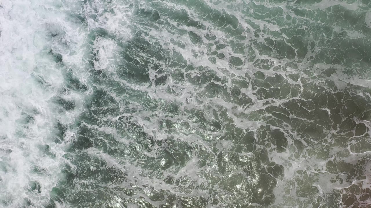Churning ocean foam and green water seen from above