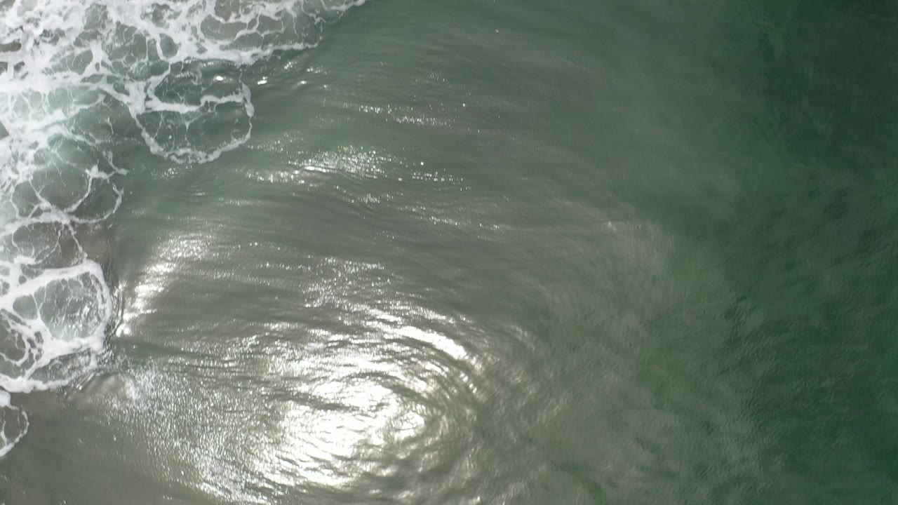 Ocean surface with white foam near the top and a large sun glare patch.