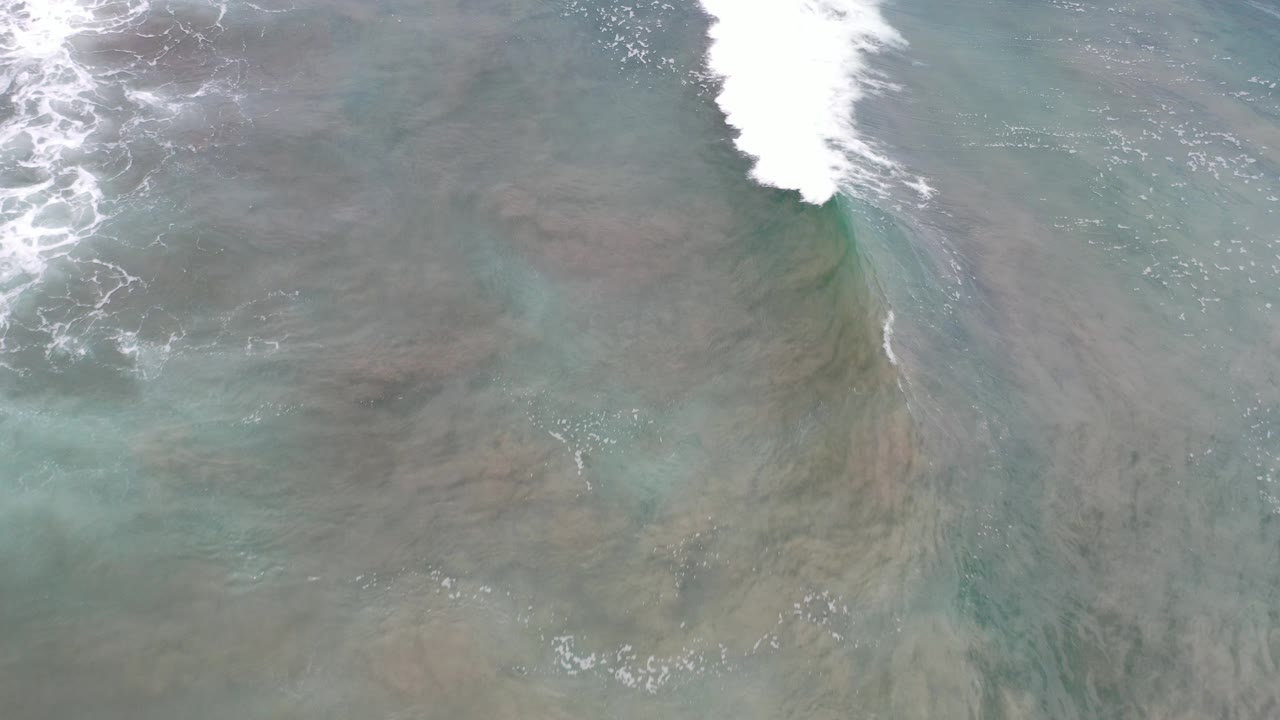 Overhead view of green-gray ocean water in Los Cabos with a white surf band entering along the top edge and no visible people.