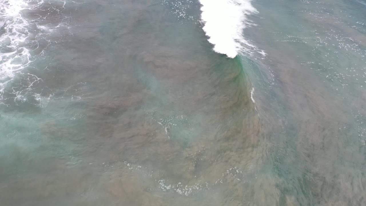 High-angle Los Cabos ocean frame with white foam spreading from the upper left over translucent green water and no visible people.