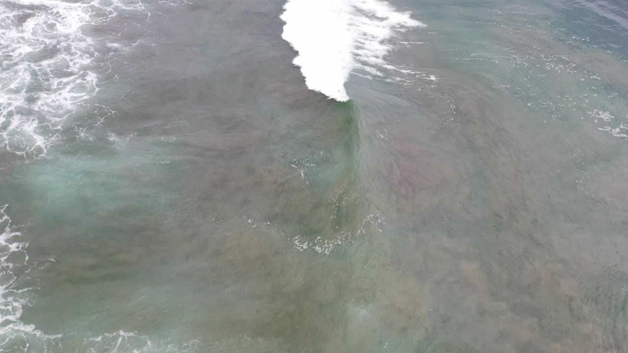 Overhead surf line breaks across muted green and gray sea.