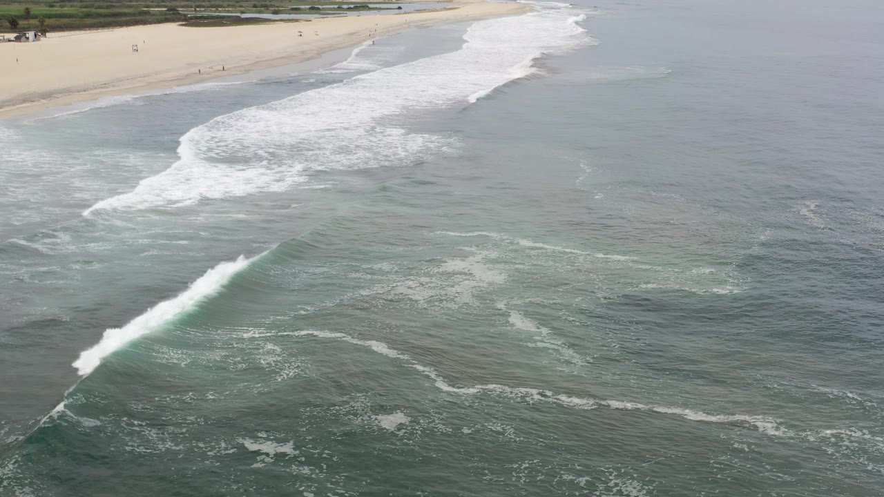 Aerial view of surf breaking beside a sandy beach.