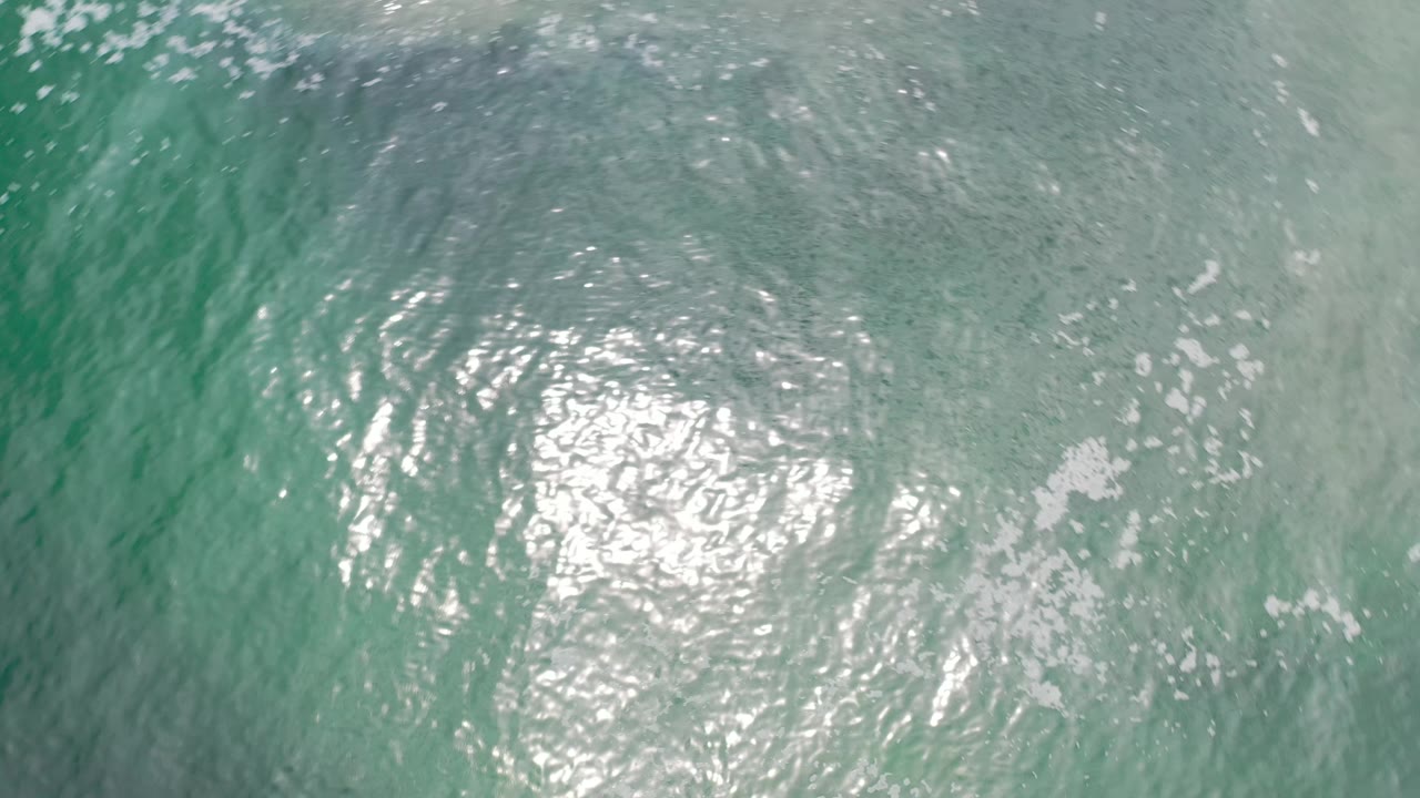 Clear green-blue water in Los Cabos, Mexico, with tight ripples around a central patch of sun glare and no visible people.