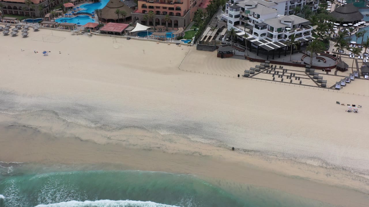 Top-down coastal view with hotel buildings and surf line.