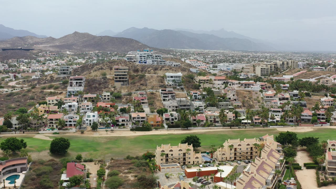 Aerial view over green field, homes, dry hills, and hazy mountains