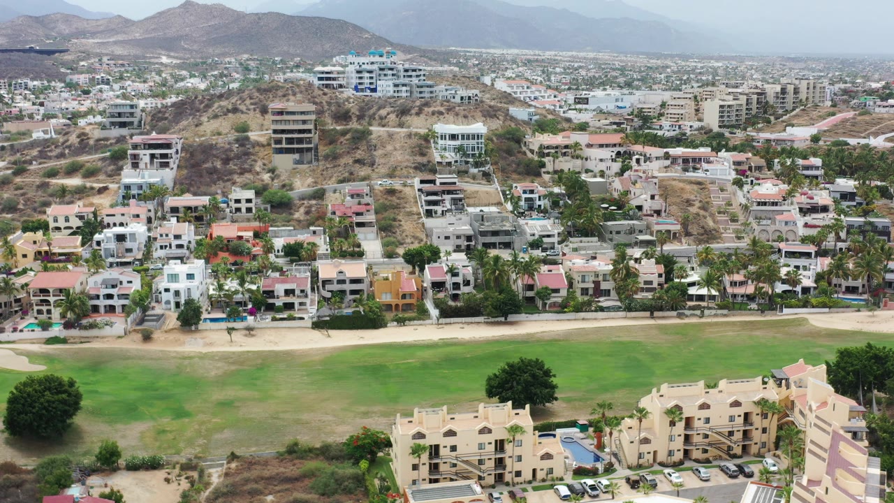 Aerial view of green open space, homes, hillside buildings, and mountains.