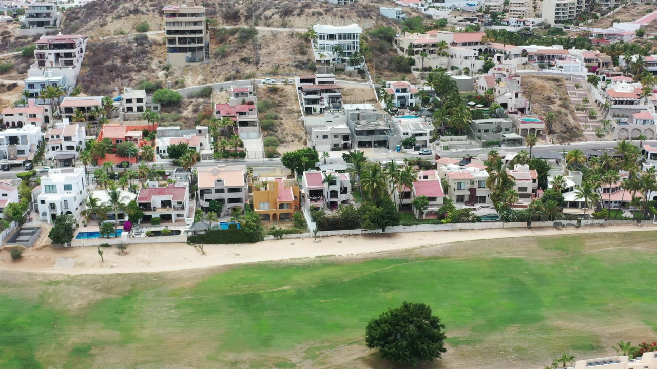 Aerial view of green space, beachfront homes, road, and hillside buildings.