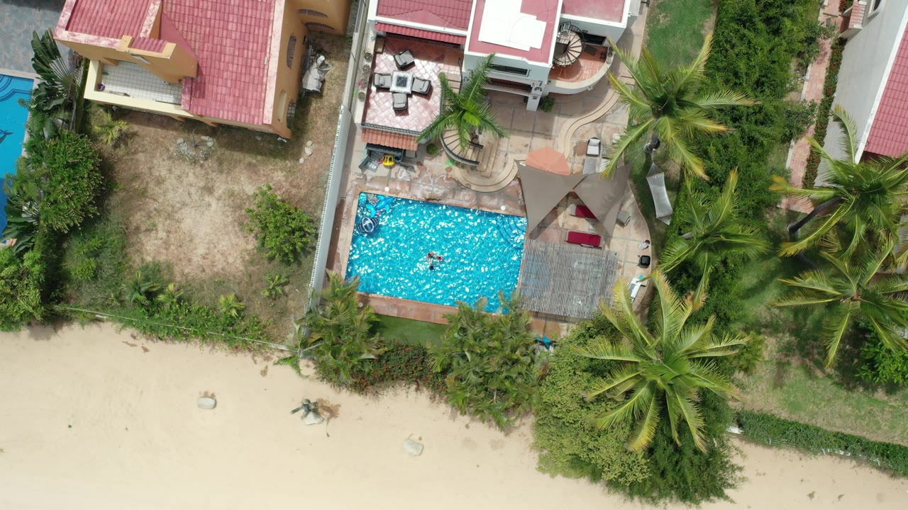 Overhead view of beach houses, pool, palms, and sand.