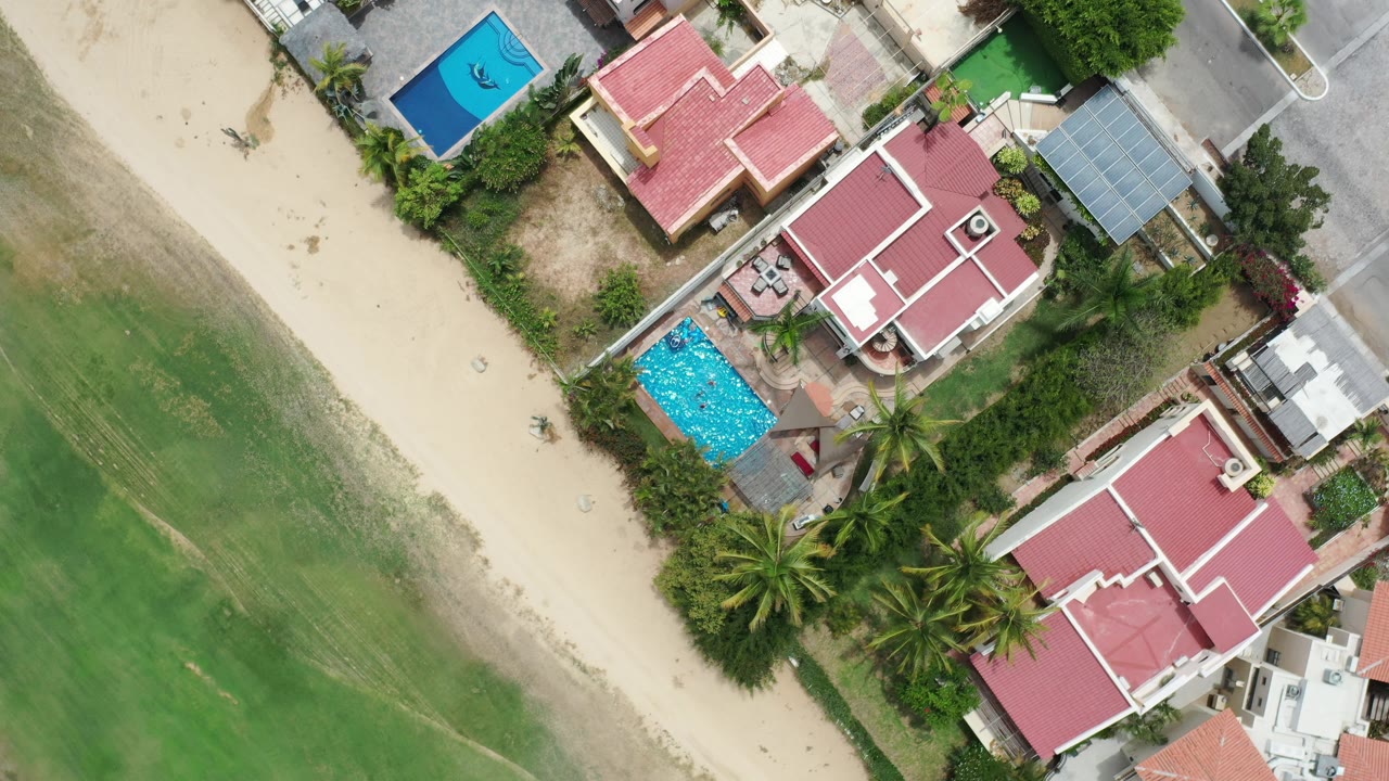 Bird's-eye view of homes and pools next to sand and green turf.