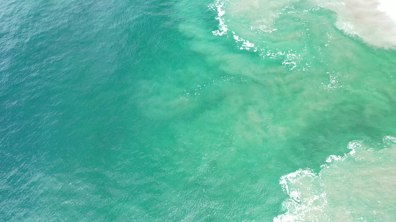 Overhead blue-green sea with foam lines along pale water.