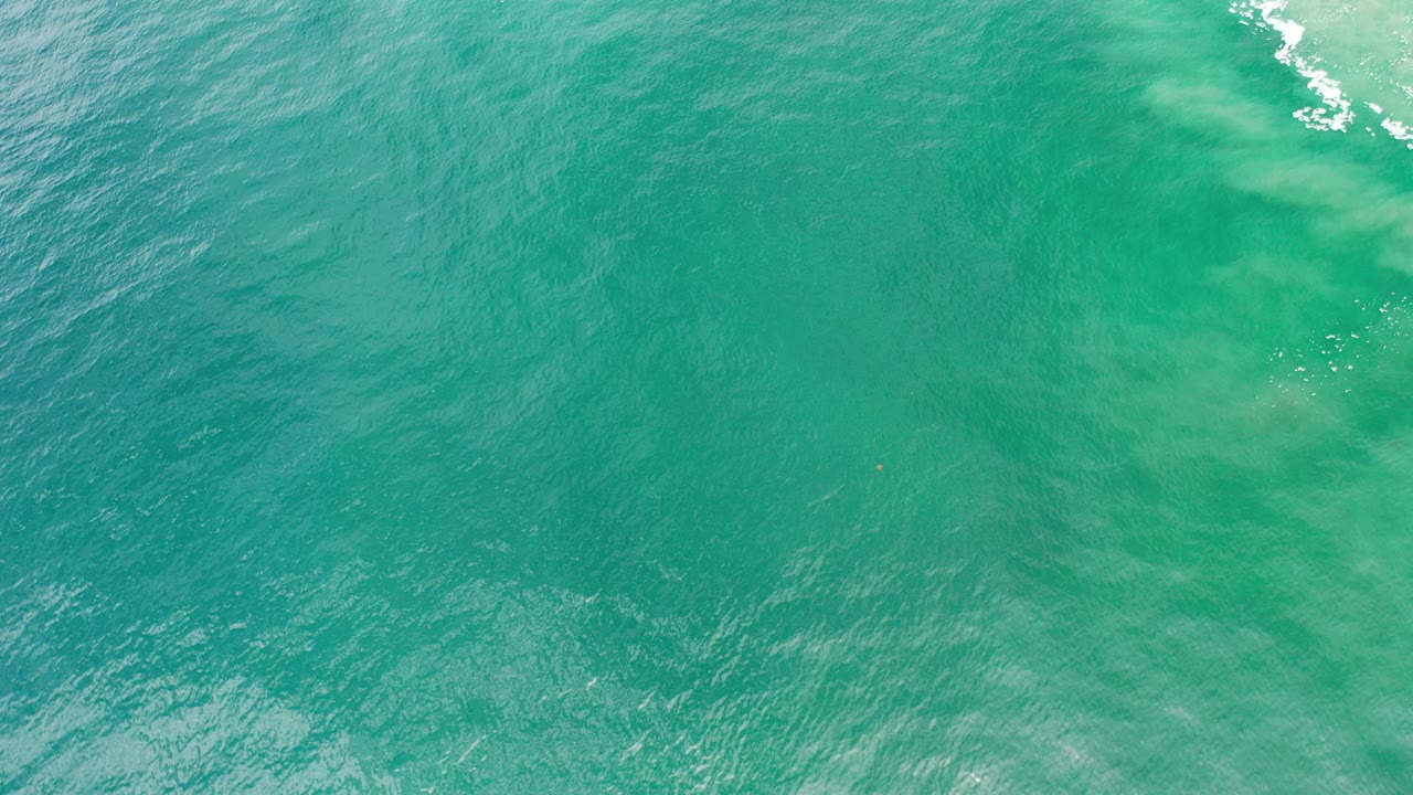 Overhead view of turquoise-green ocean water in Los Cabos, Mexico, with faint lighter patches below the surface and no visible people.
