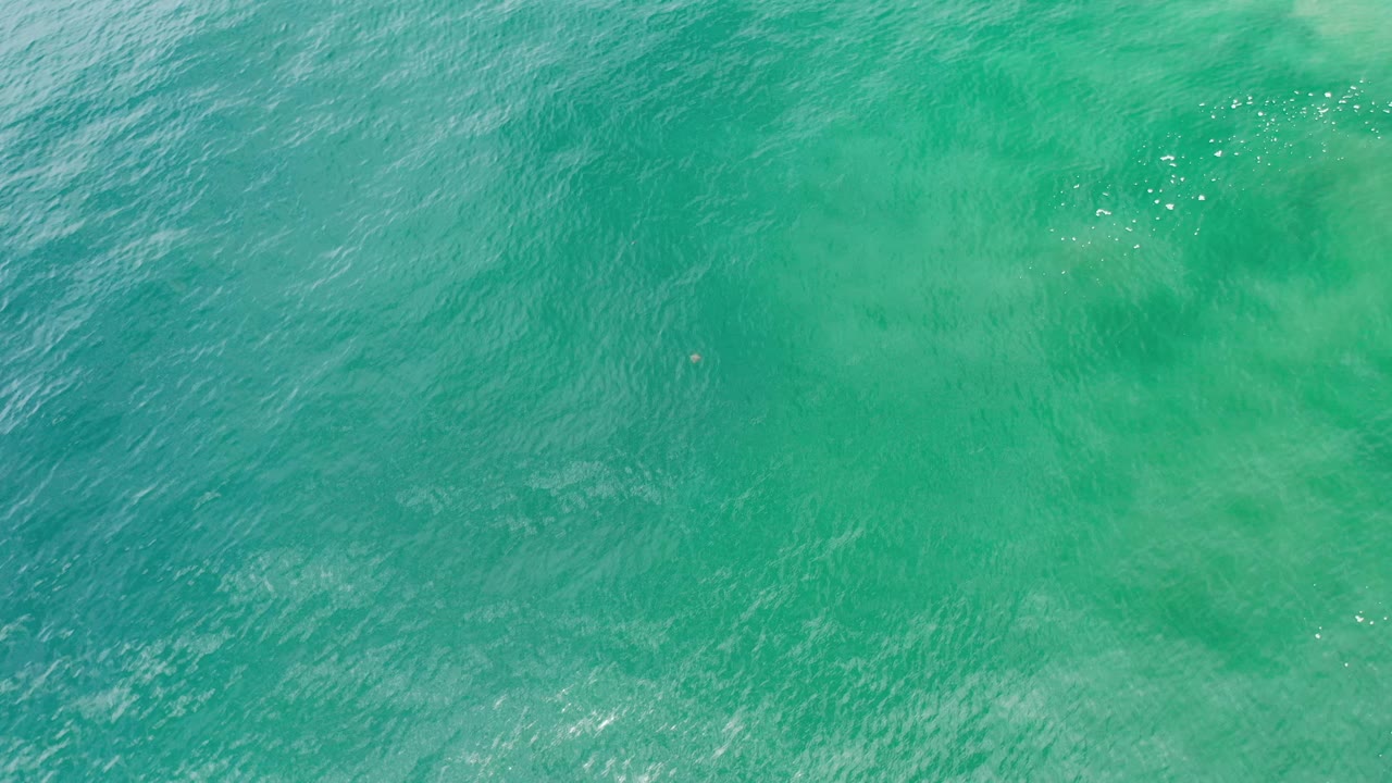 Aerial ocean texture with turquoise water and pale clouded patches.