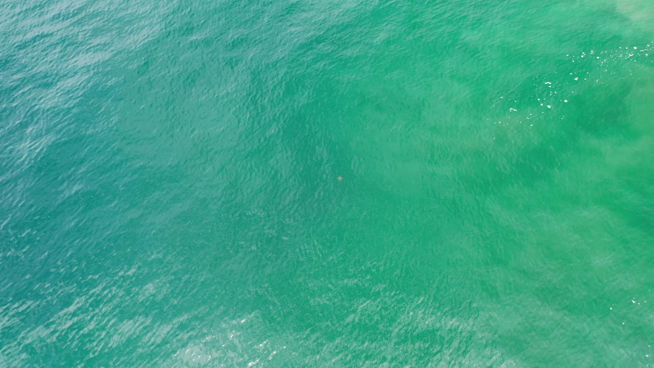 Overhead view of blue-green ocean water in Los Cabos, Mexico, with subtle ripples and pale underwater patches, no visible people.