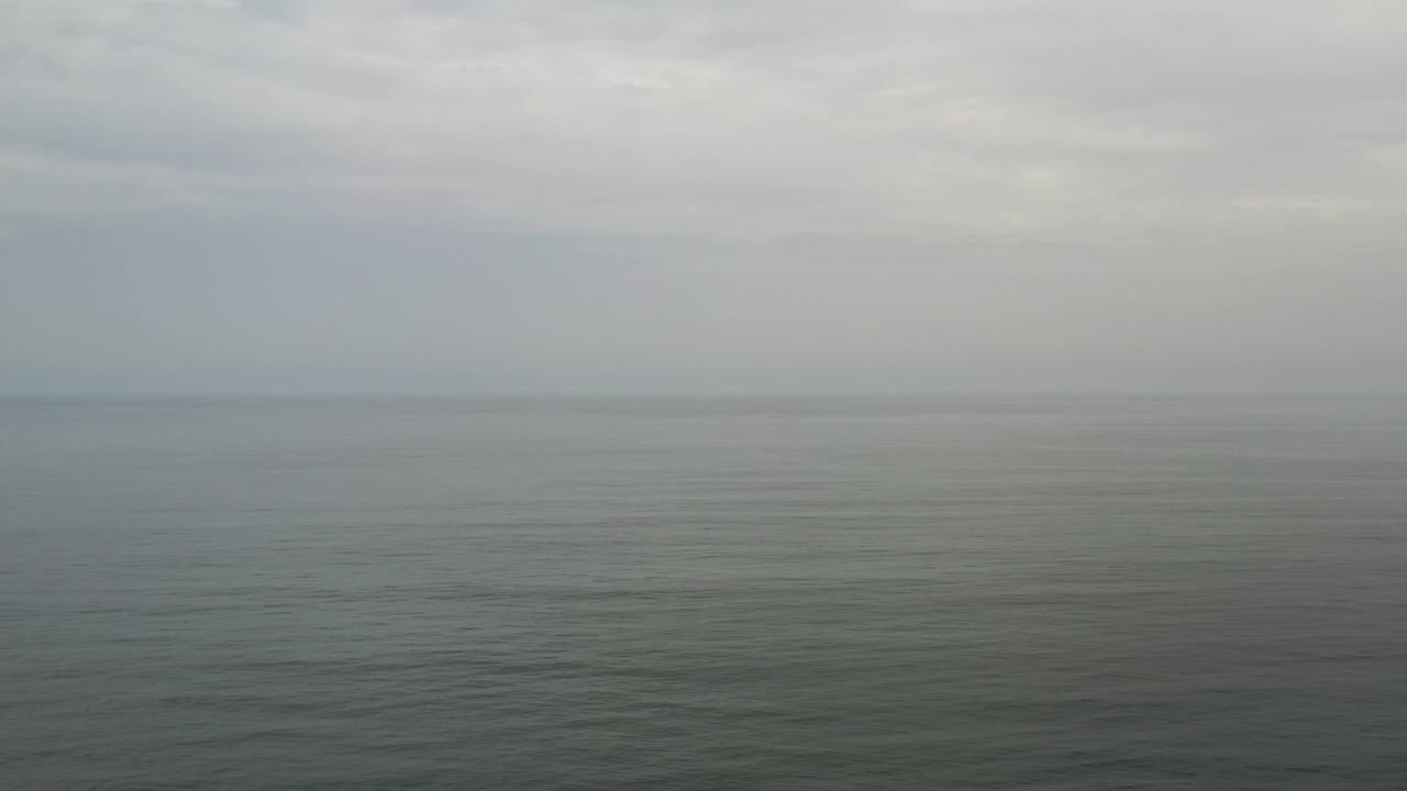 Opening frame of Los Cabos ocean water under a hazy cloudy sky, with a faint horizon and no visible people.