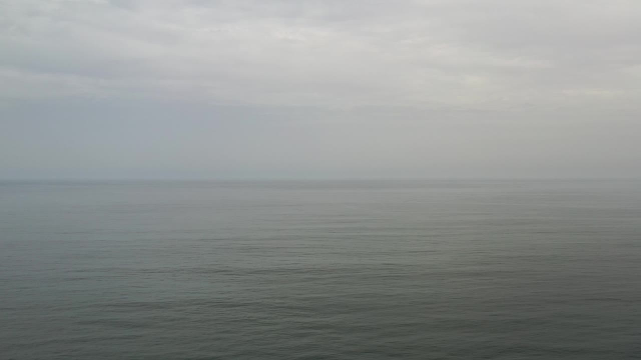 Hazy ocean horizon with subdued gray clouds.