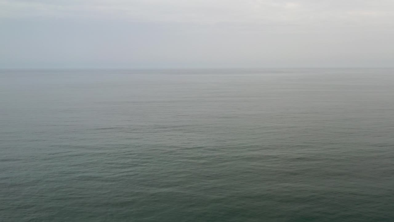 Opening frame of gray-green ocean water in Los Cabos, Mexico, with a pale fog band at the horizon and no visible people.