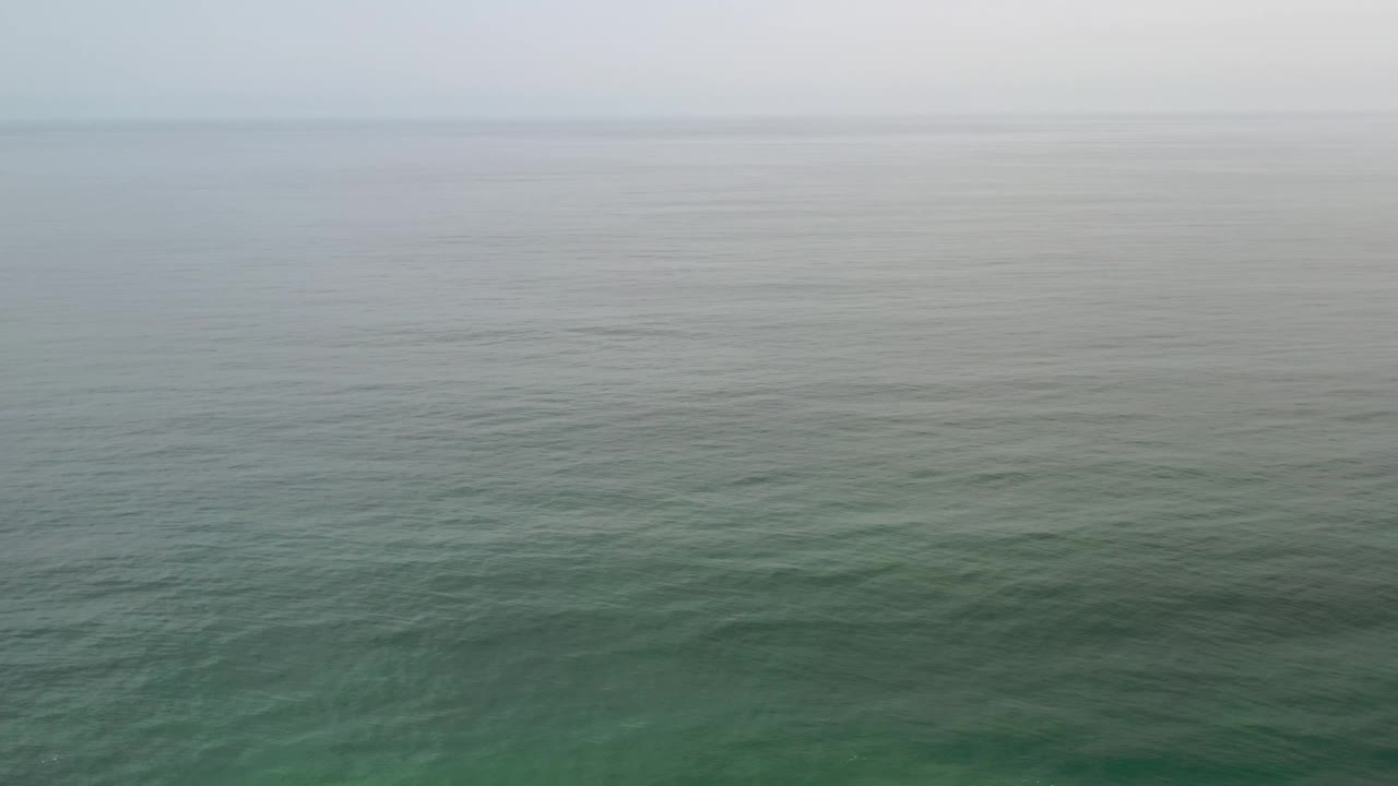 Open Los Cabos sea fills the frame beneath a pale cloudy horizon, with faint ripples and no visible people.