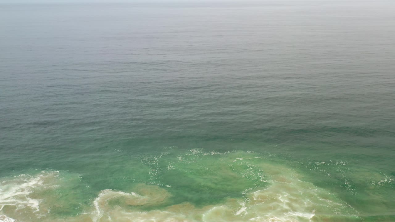 Aerial view of green-blue ocean and white surf near shore.