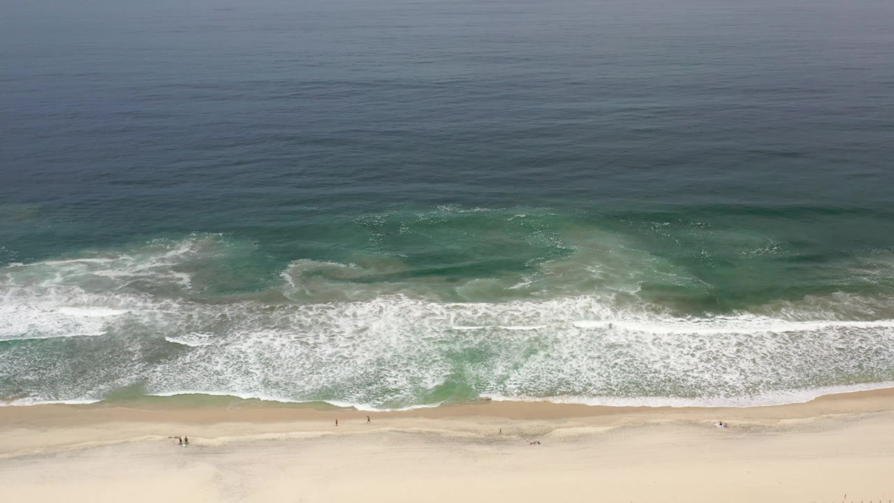 Drone view of white surf rolling toward an empty beach.
