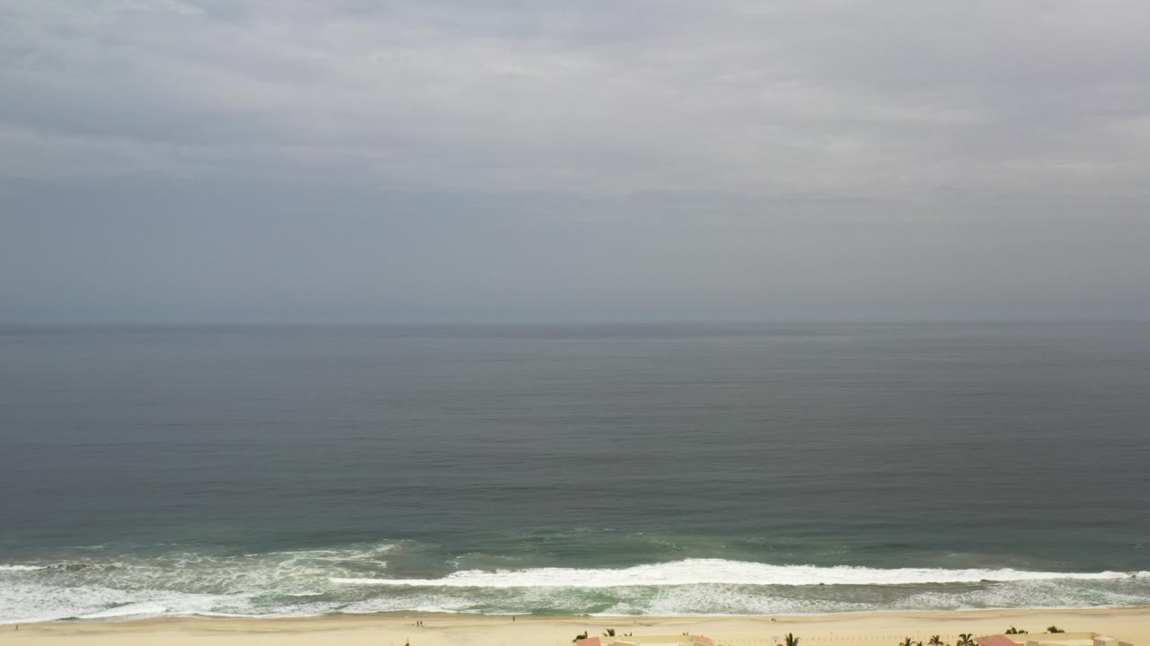 Cloudy ocean horizon over waves breaking on a sandy beach.