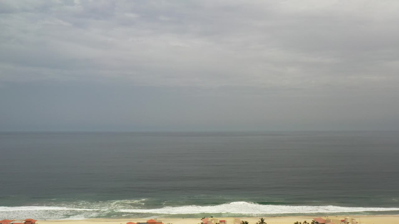 Wide gray ocean horizon above a beach and low red-roofed buildings.