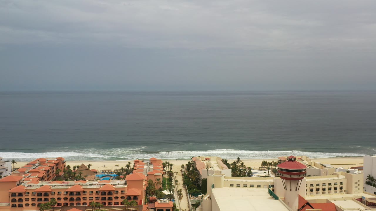 Wide coastal view with ocean, beach, hotels, and rooftops.