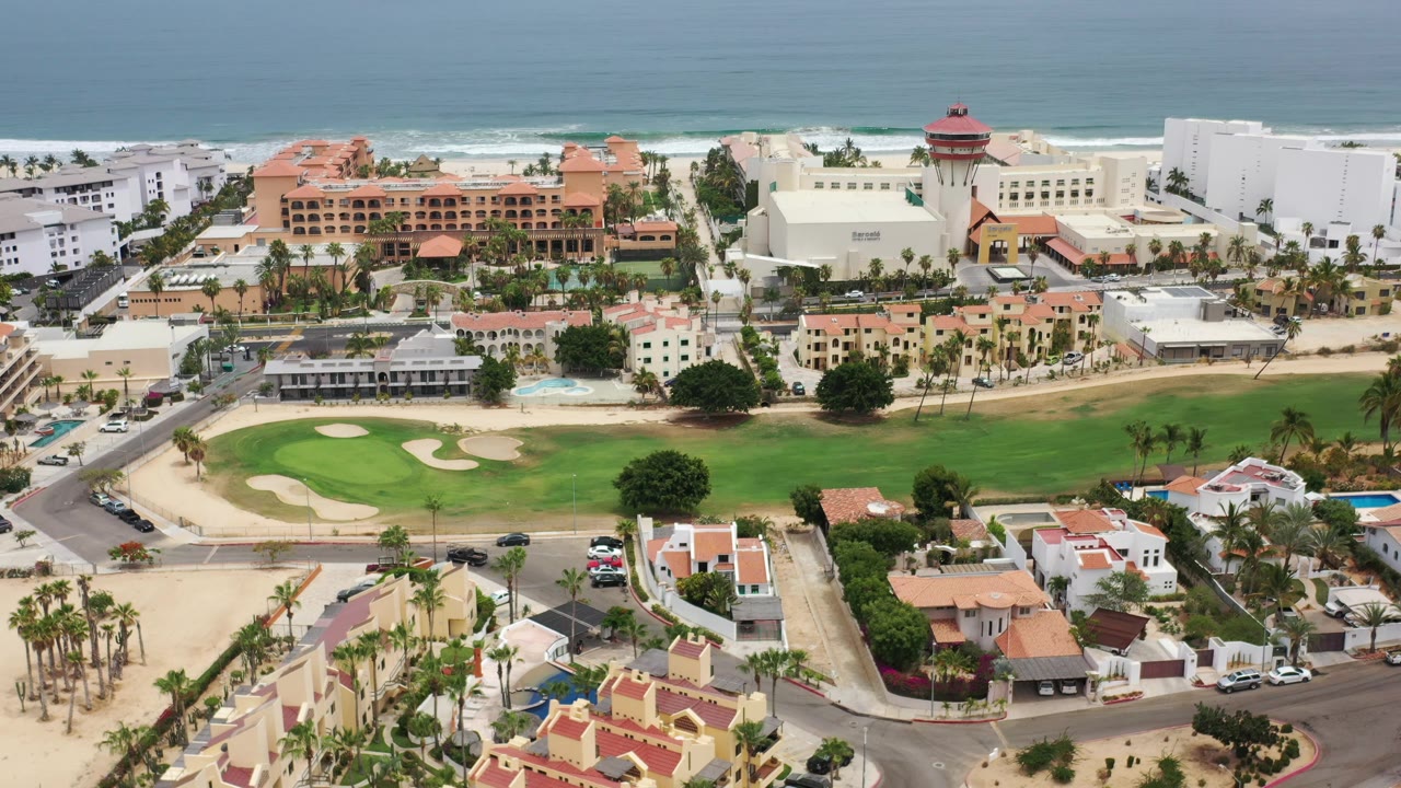Drone view across roads, villas, golf green, and beachfront buildings.