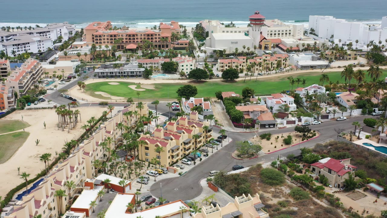 Aerial view of coastal buildings, roads, lawns, and ocean horizon.