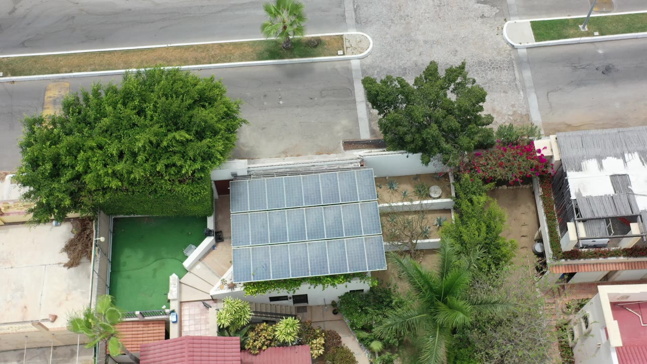 Aerial view of small building beside trees, palms, walls, and a quiet road.