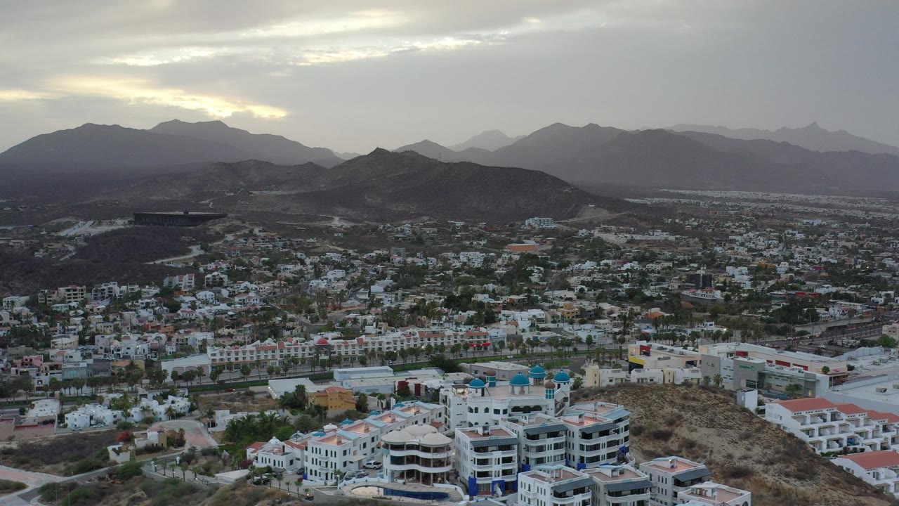 Aerial view of a town below dark hills and a cloudy sunset sky.