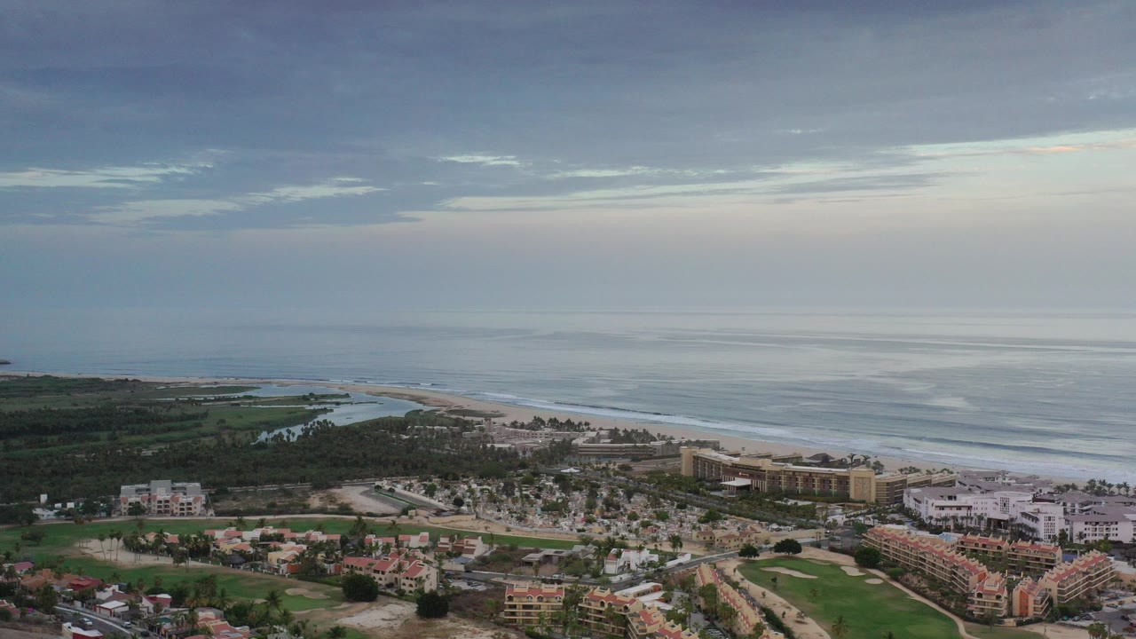 Aerial view of coastal buildings, beach, ocean, and cloudy sky.