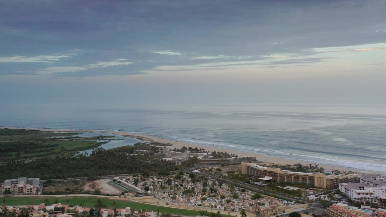 Wide aerial view of coastline, ocean, beach, greenery, and buildings.