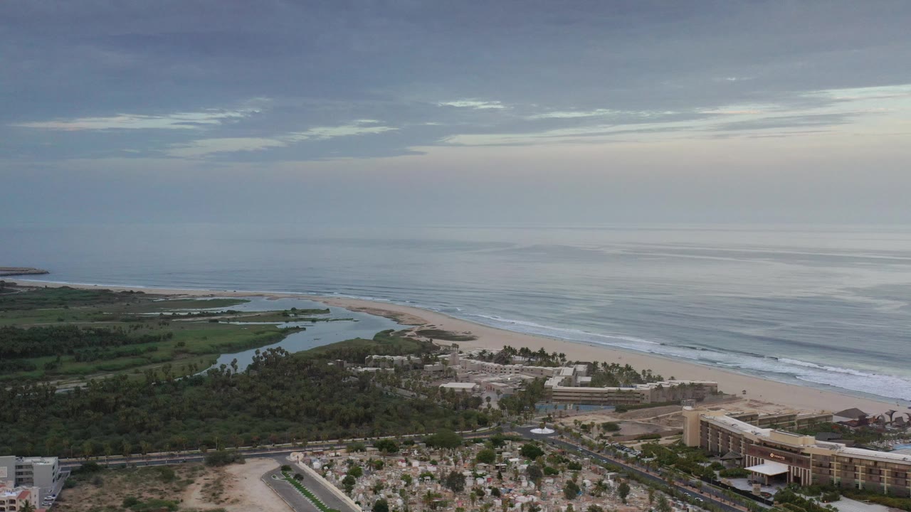 Drone-like coastal wide shot with ocean horizon, beach, lagoon, and resort-area buildings.