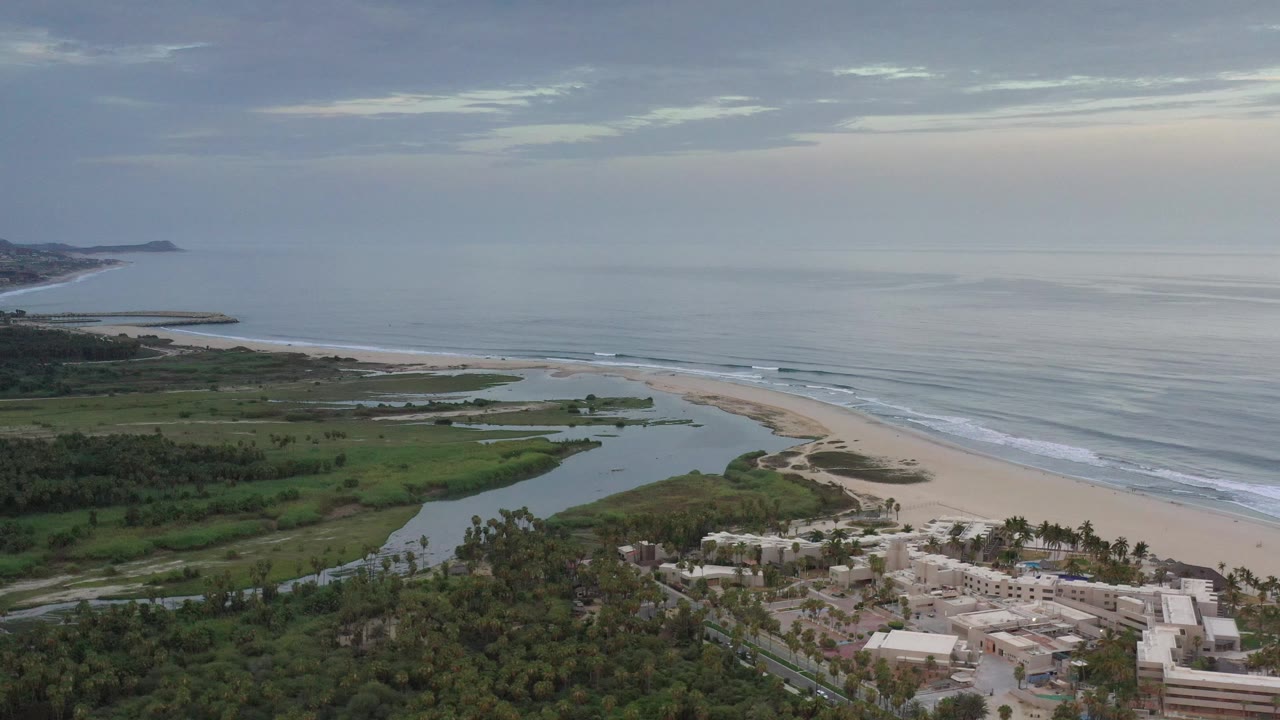 Aerial coastline with beach, lagoon, trees, buildings, and gray-blue ocean.