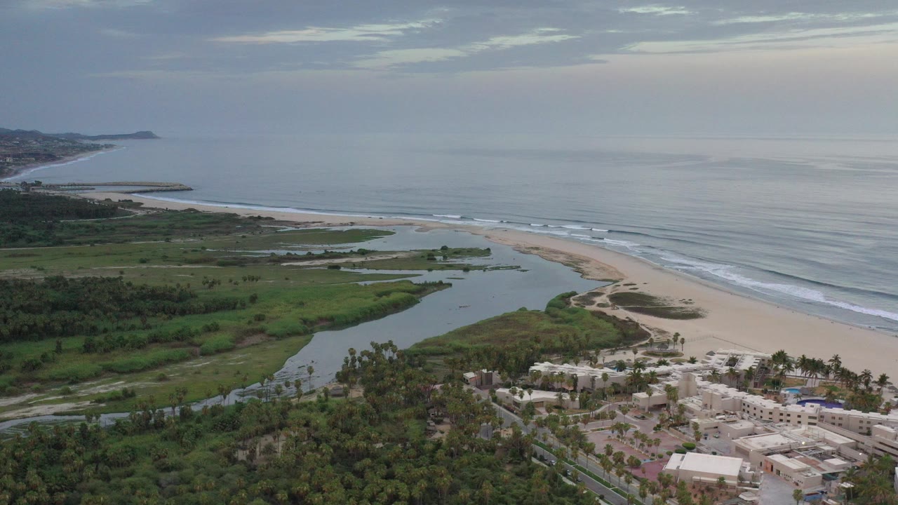 Aerial view of a river mouth, beach, ocean, and coastal buildings.