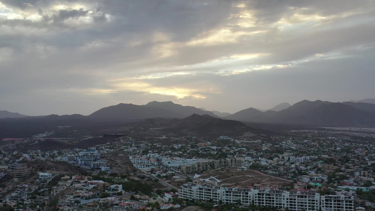 Aerial city view below dark mountains and a cloudy sky.