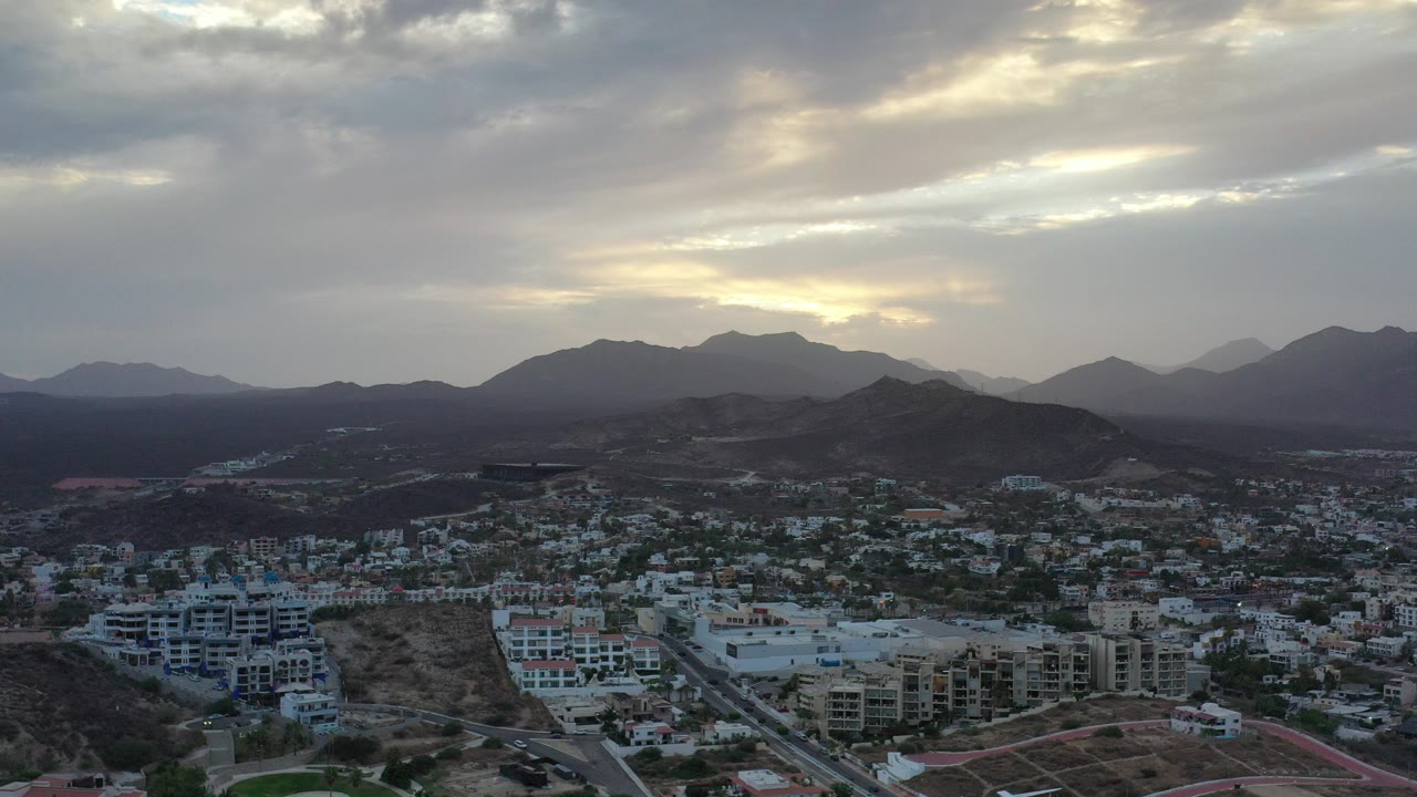 Aerial view of town buildings below mountains under a cloudy sky.