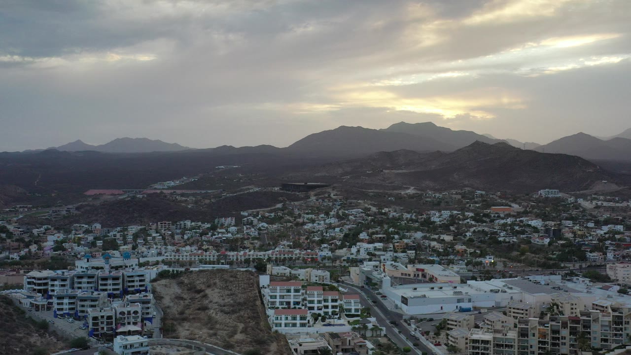 Aerial view of buildings below dark hills at sunset.