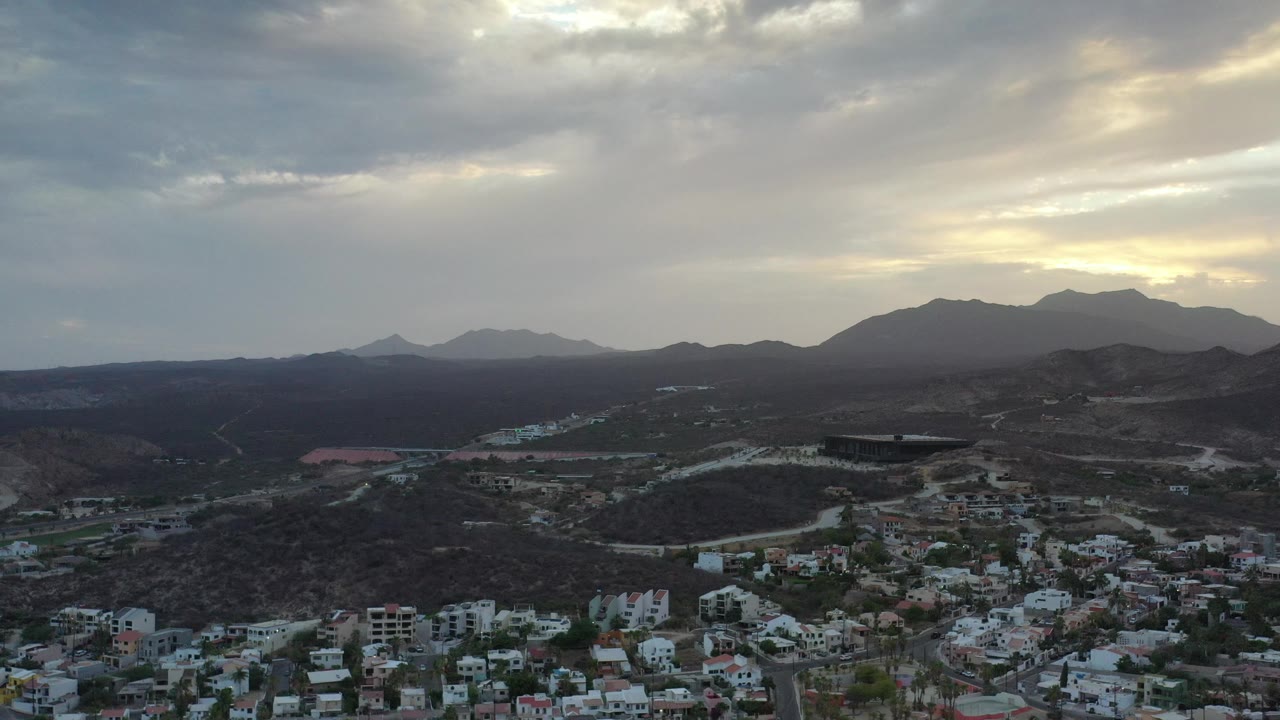 Town edge and mountain range seen from above beneath layered clouds