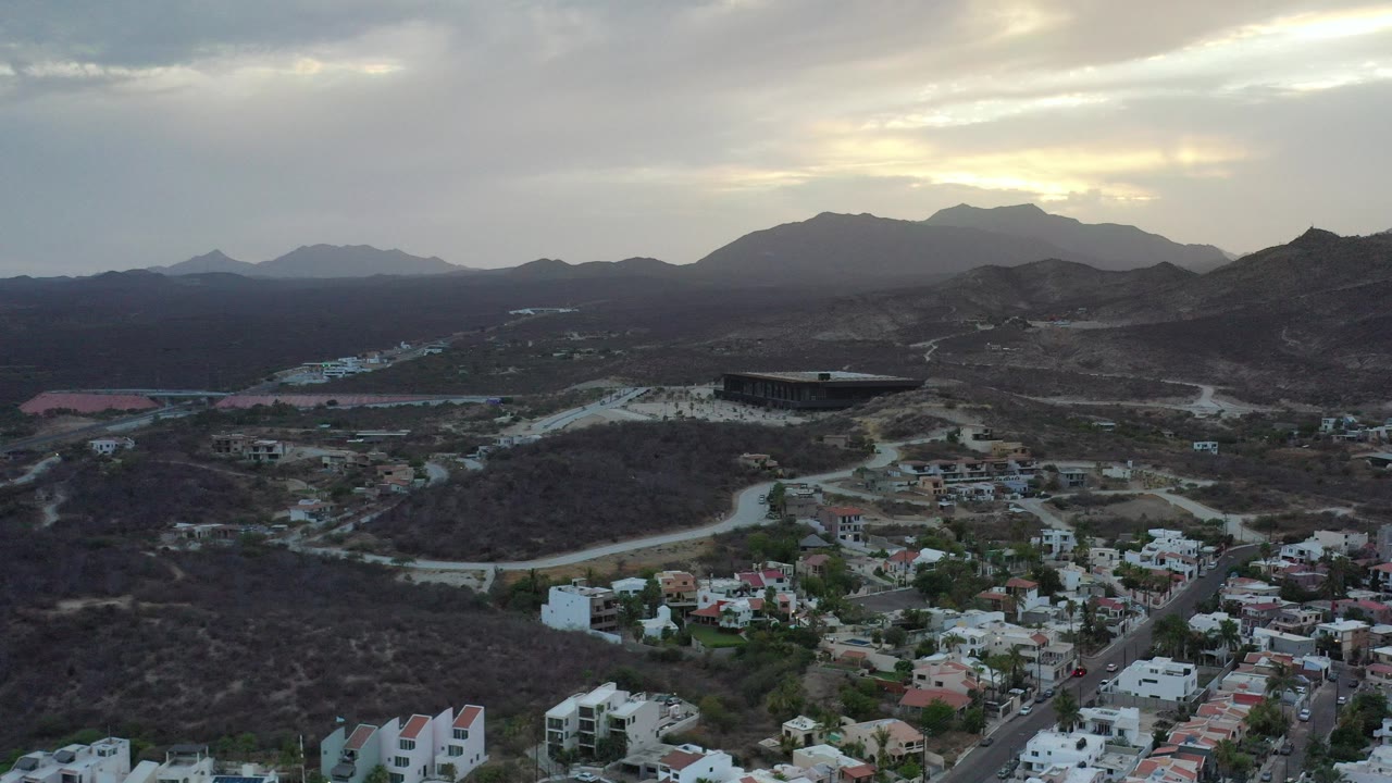 Aerial view of homes, dirt roads, dry hills, and mountains under cloudy light.