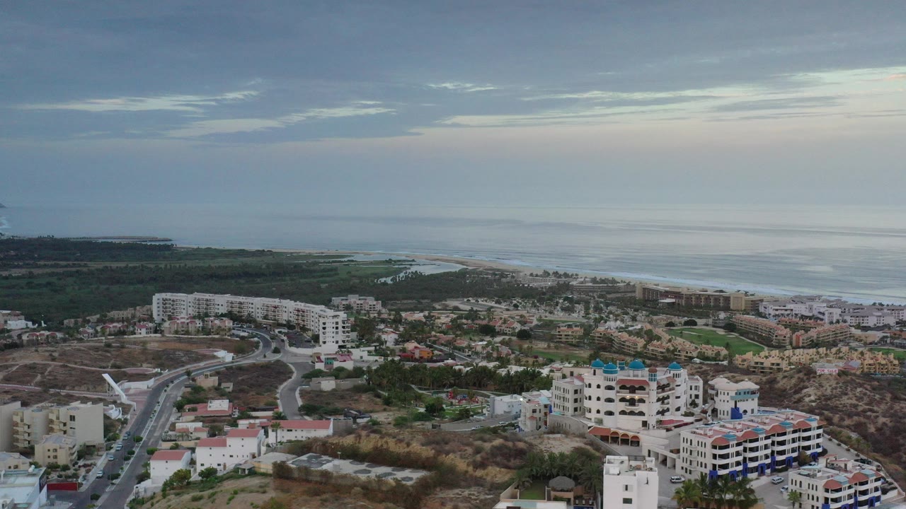 Aerial view of coastal buildings, roads, beach, and ocean under cloudy sky.