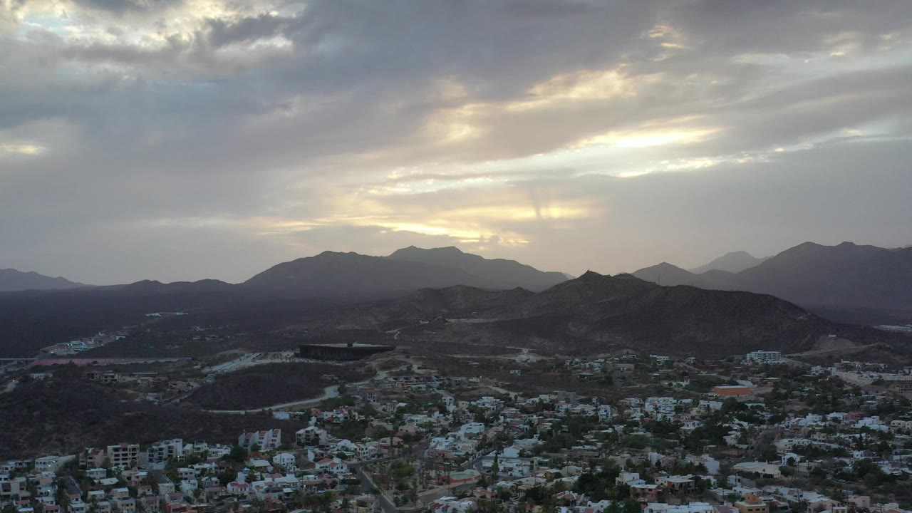 Mountain ridges behind a low residential area under bright clouds.
