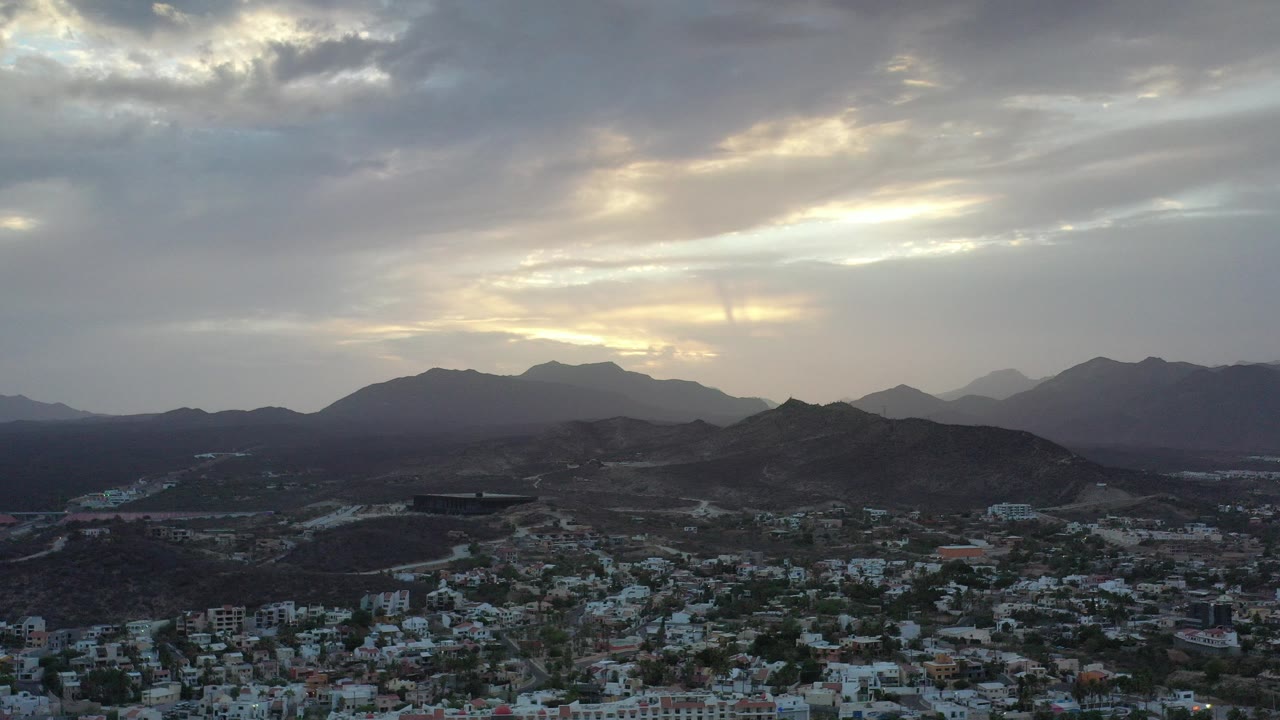 Aerial view of a town below dark hills and cloudy sky.