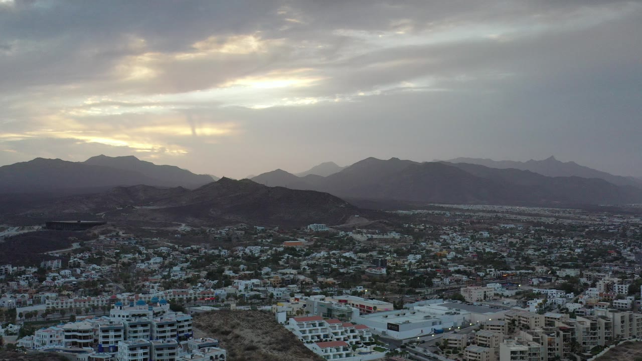 Elevated city view with mountains under cloudy sky.