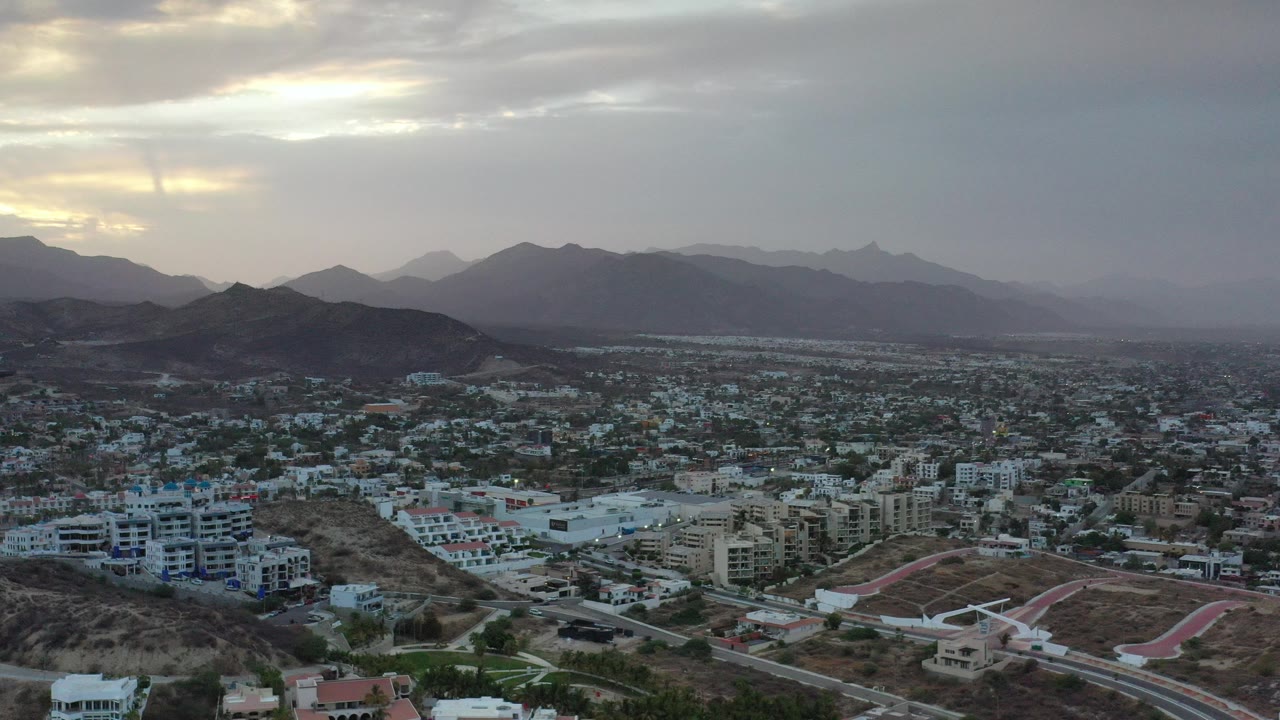 Aerial view of a city below dark mountains and cloudy sky.