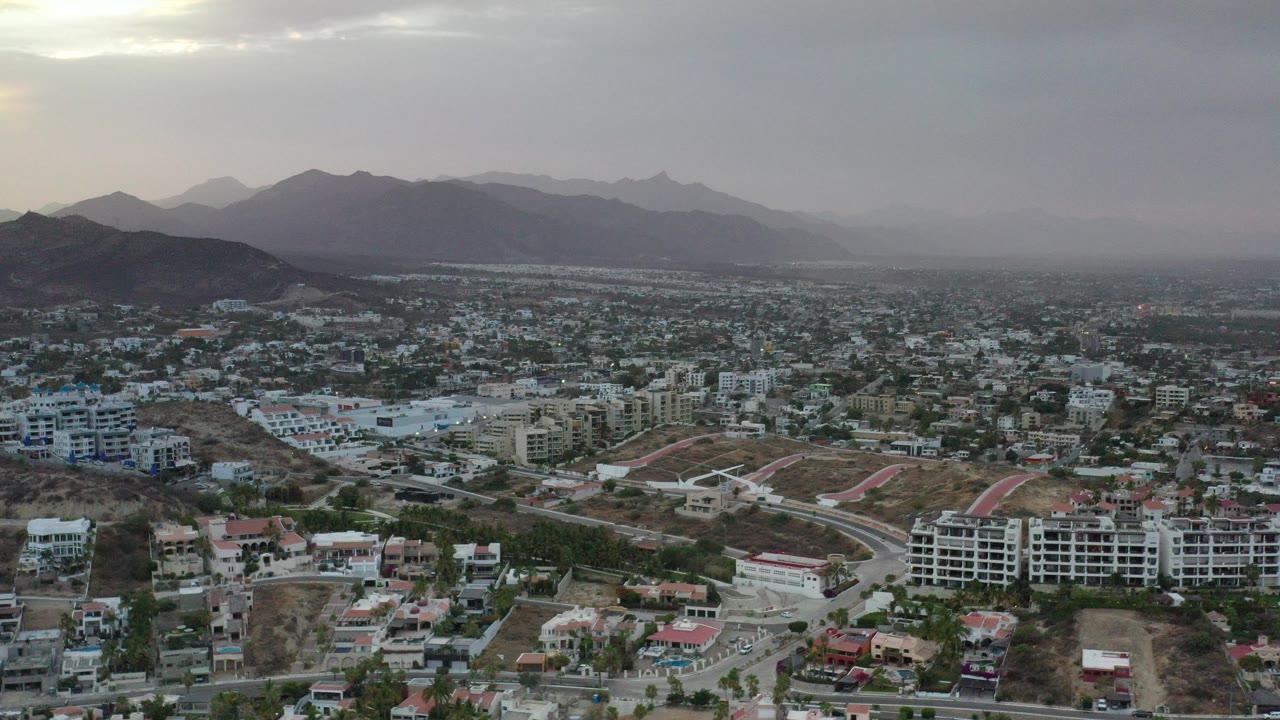 Aerial view of a suburban city below cloudy mountains.