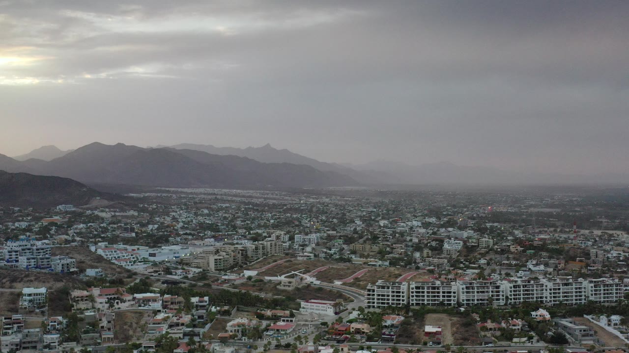 Aerial view of a hazy city below gray clouds and distant mountains.