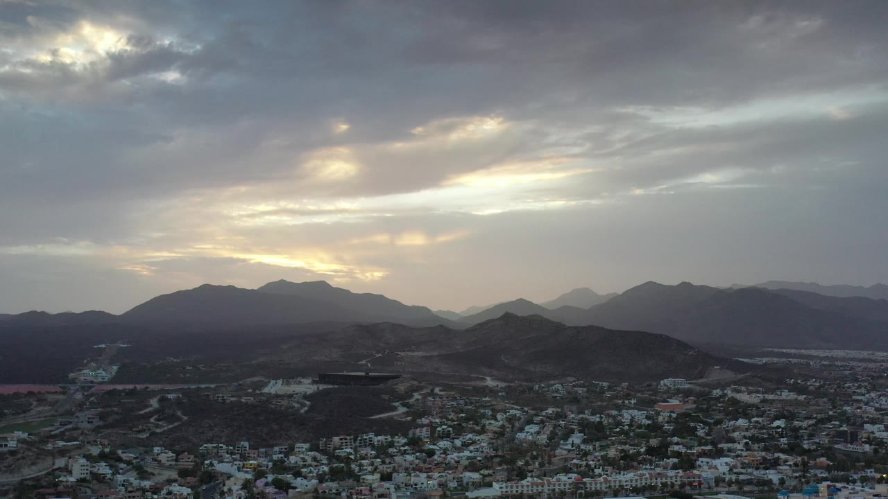 Dark hills and town rooftops under a bright cloud opening.