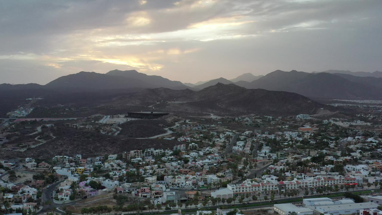 Elevated city view with mountains silhouetted beneath bright clouds.
